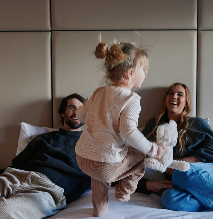 little girl jumping on bed with parents