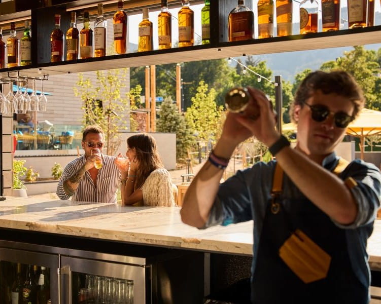 A couple sitting at a bar drinking a cocktail with a bartender shaking a drink