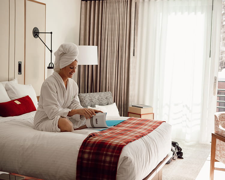 woman on bed smiling and reading in white robe