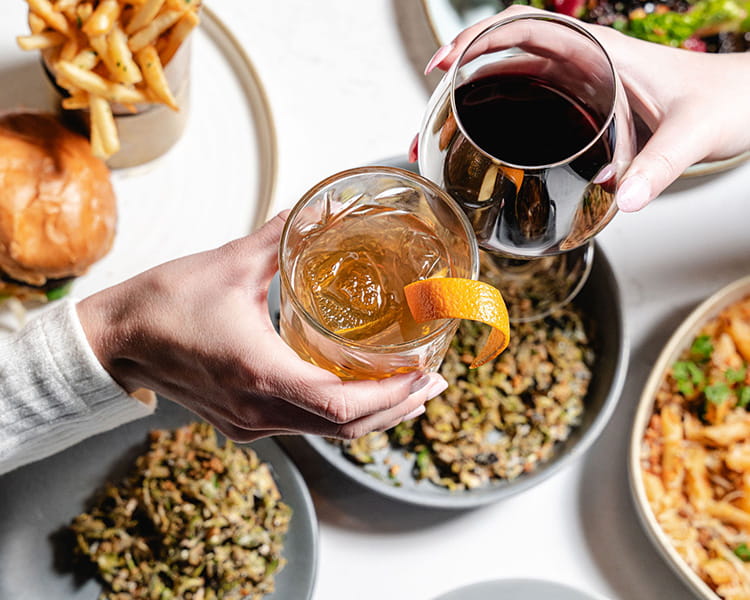 two hands cheerings drinks over table of food at ajax downtown