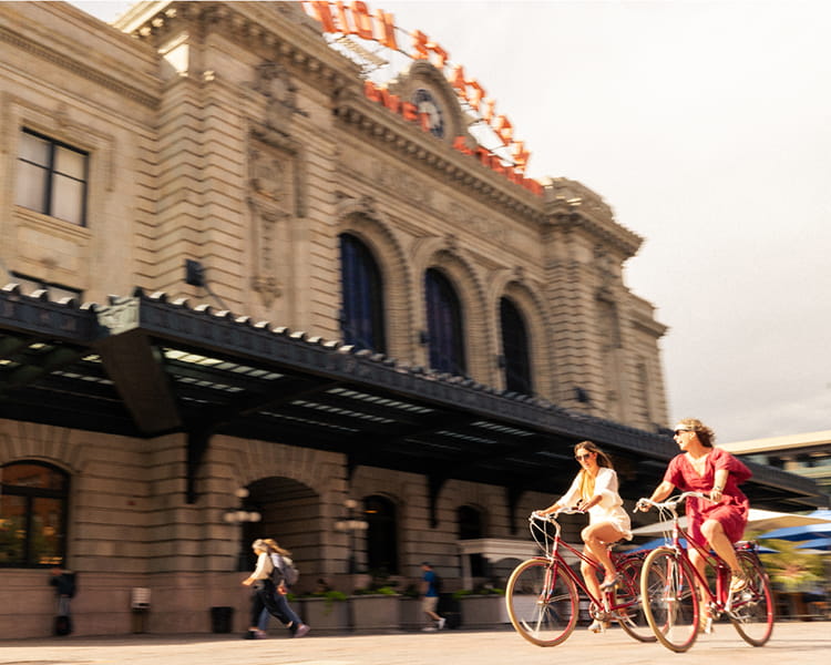 two people riding bikes in front of denver union station