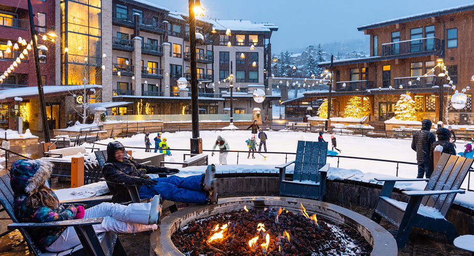people sitting around fire in front of ice skating rink in snowmass village
