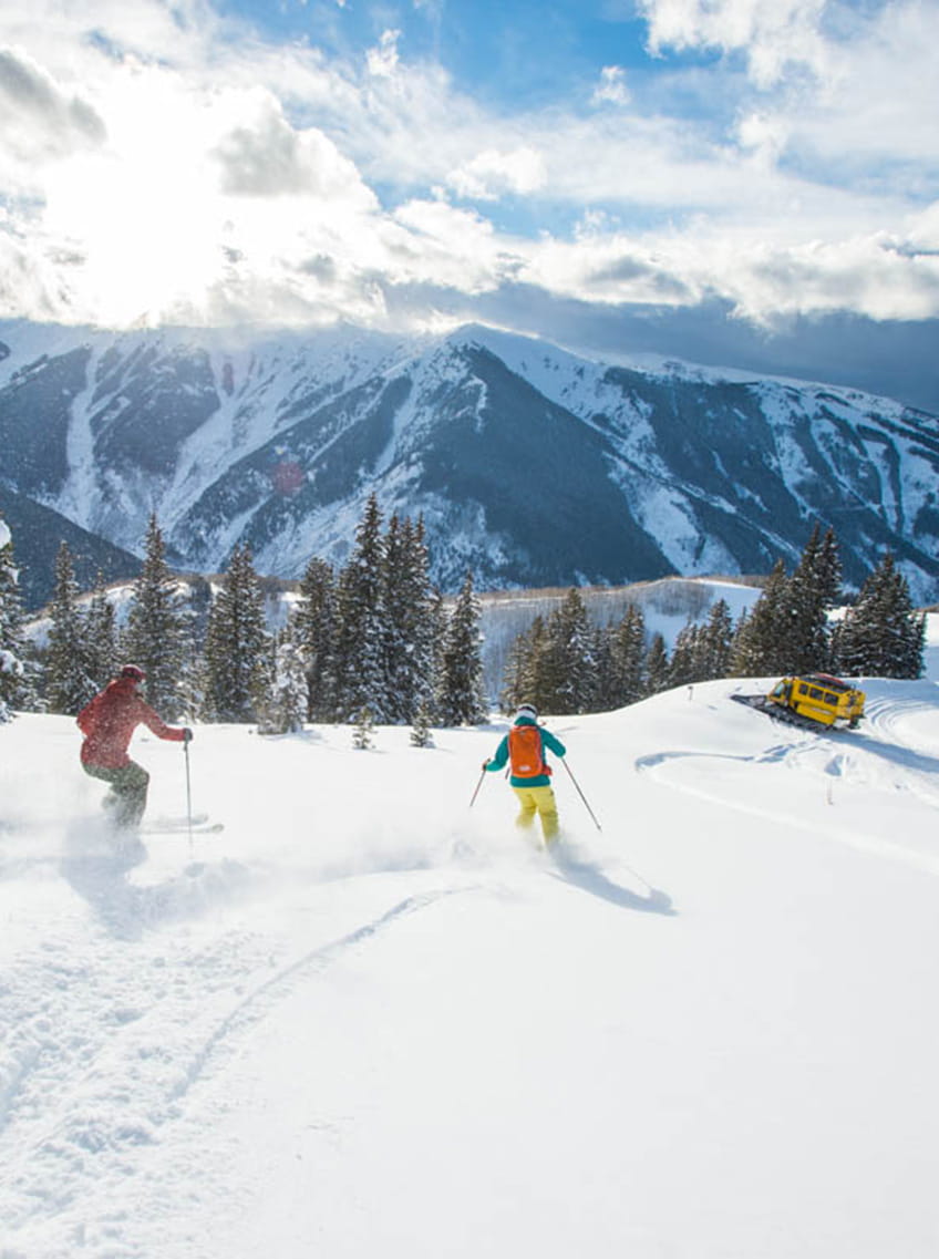 two skiers skiing toward snow cat on mountain