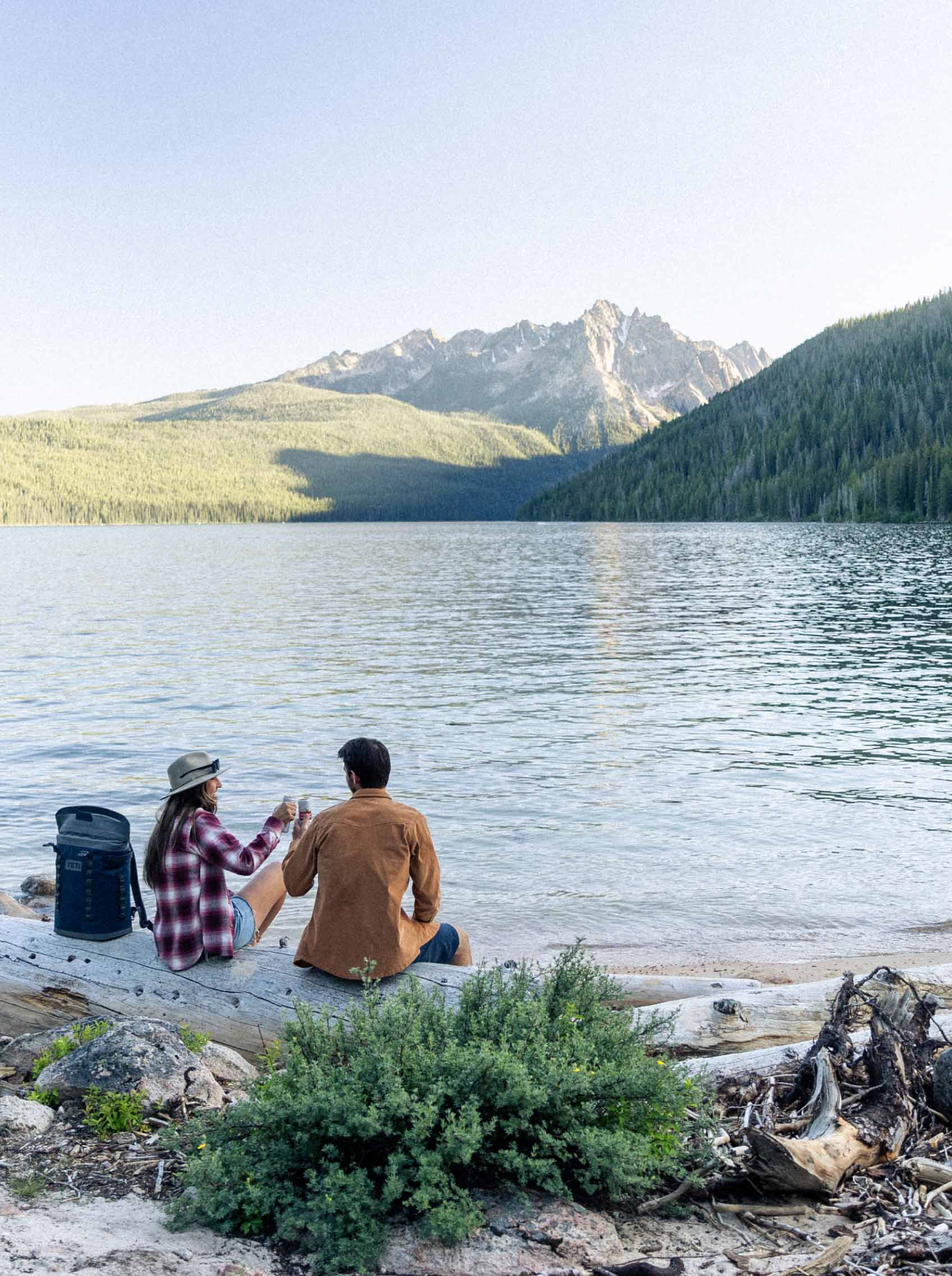 couple sitting by lake and mountains