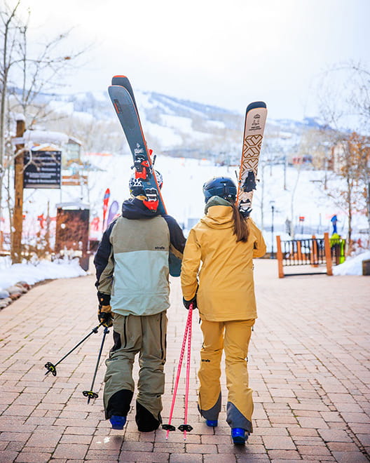 Two skiers walking around Snowmass base