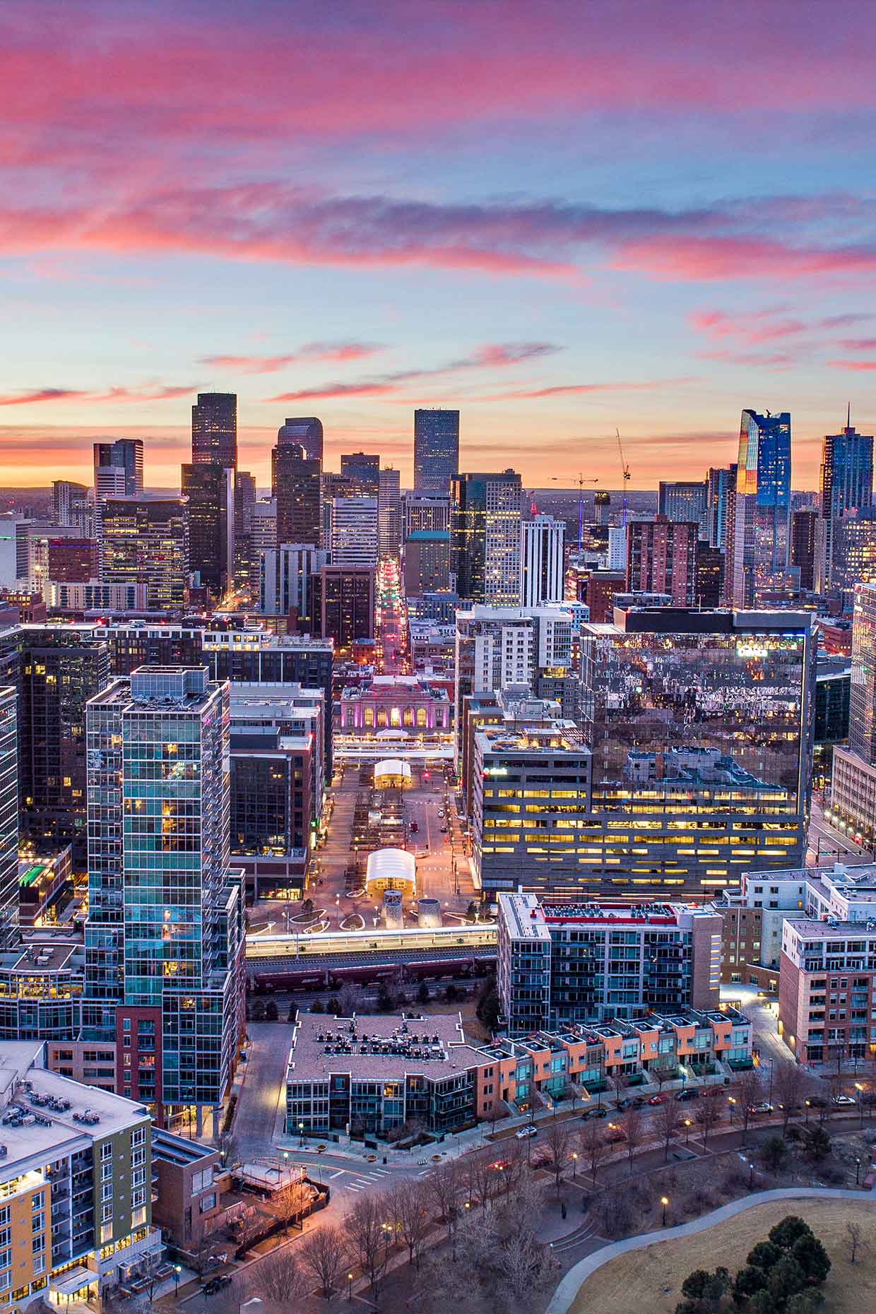Denver’s downtown street with lit skyscrapers at dusk, featuring a stunning sunset in pink and purple hues creating a vibrant skyline.