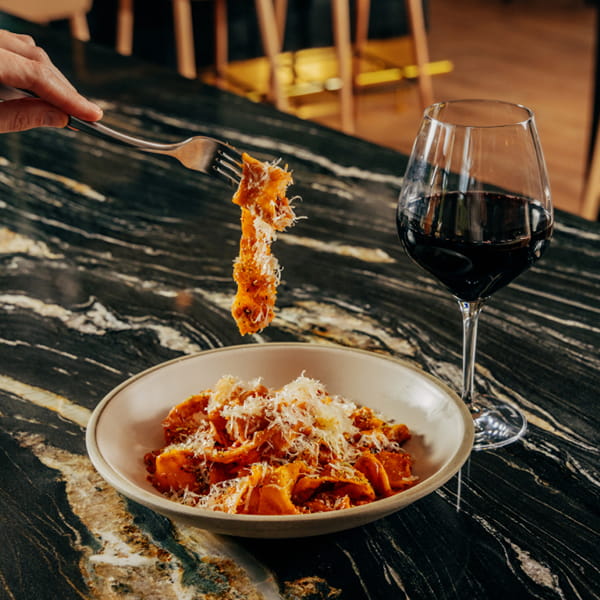 hand with fork eating pasta next to wine glass