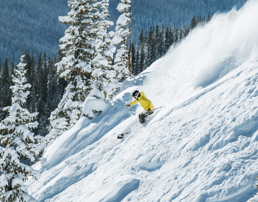 Skier in yellow jacket skiing through powder on a ski mountain