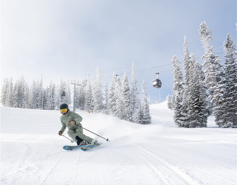 Skier in green outfit skiing on Aspen mountain through trees