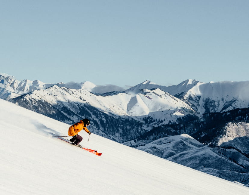 Skier in orange outfit skiing on a clear ski slope down a mountain