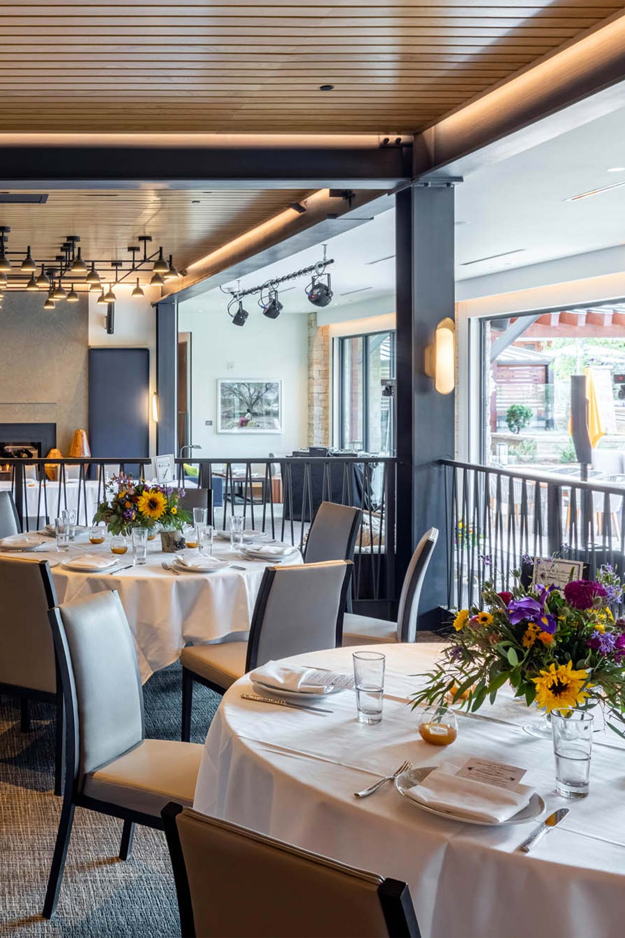 Snowmass wedding venue with tables set in white linens, floral centerpieces, modern lighting, and large windows offering indoor-outdoor views.