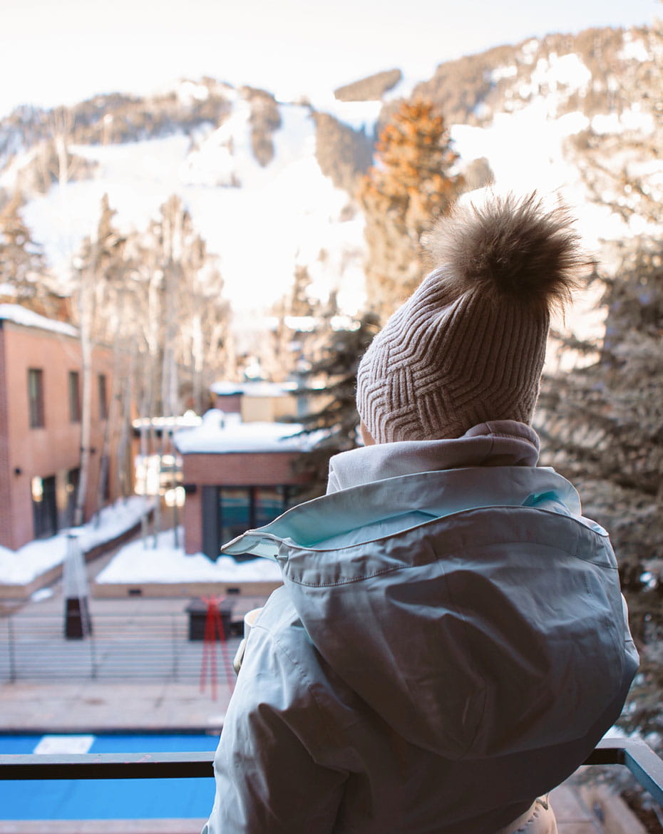 person in winter outerwear on terrace looking at mountain