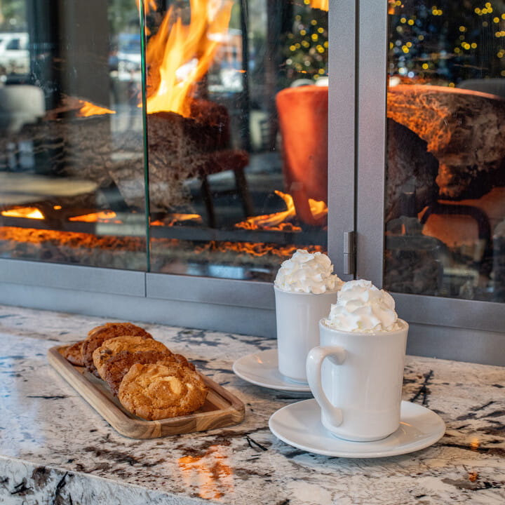 Plate of cookies and 2 hot cocoas by a fireplace