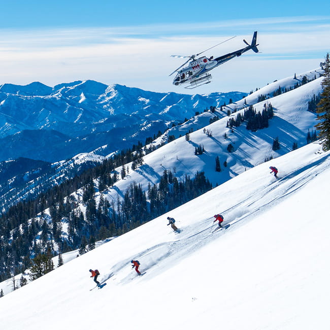five skiers skiing backcountry lines under helicopter