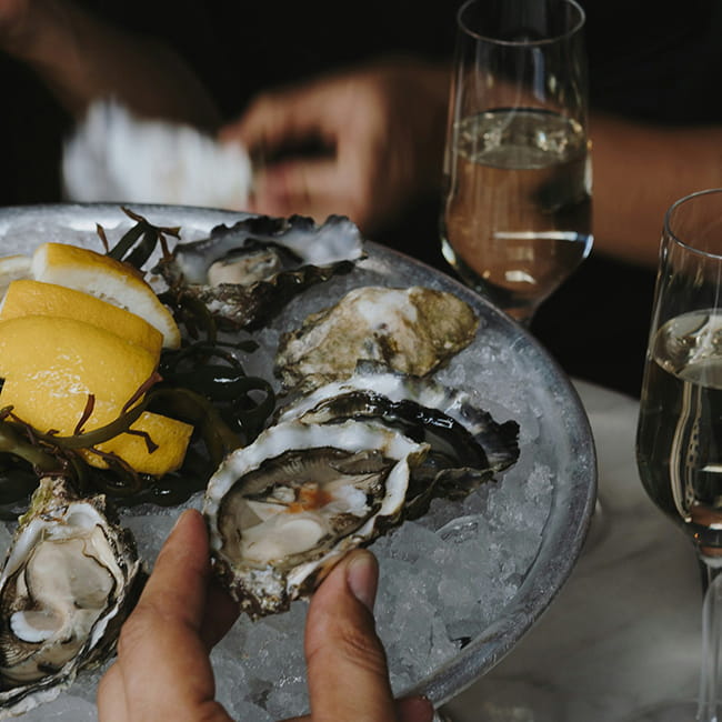 hand picking up oyster in front of white sparkling wine
