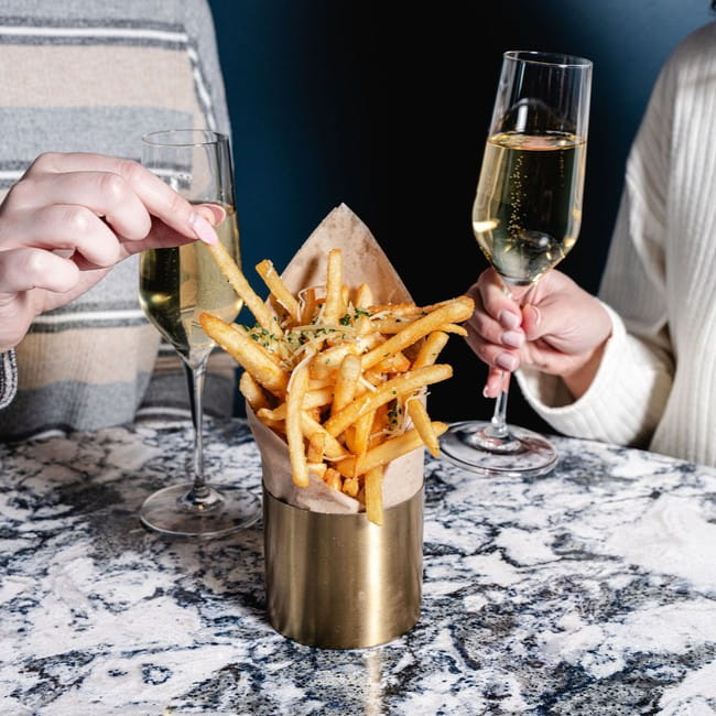 Two people will glasses of bubbly and fries at a restaurant