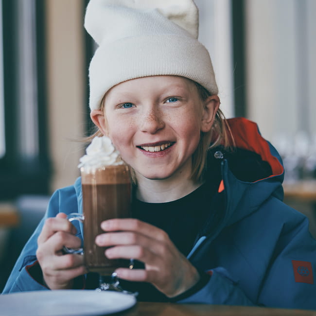 Boy smiling with hot cocoa wearing a beanie and ski jacket