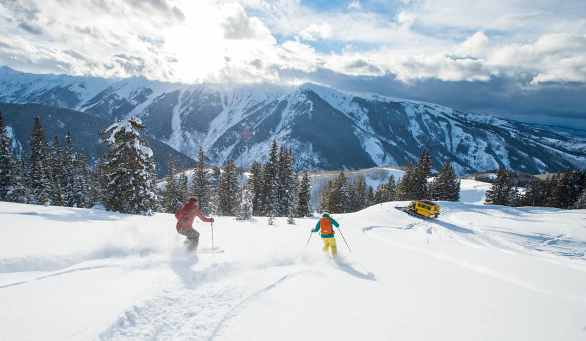 two skiers skiing on mountain toward snow cat