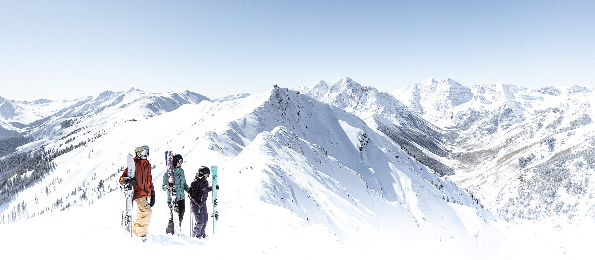 three skiers looking out at Aspen mountain range