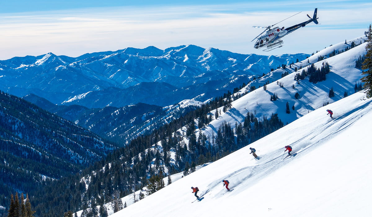 five skiers skiing backcountry lines under helicopter