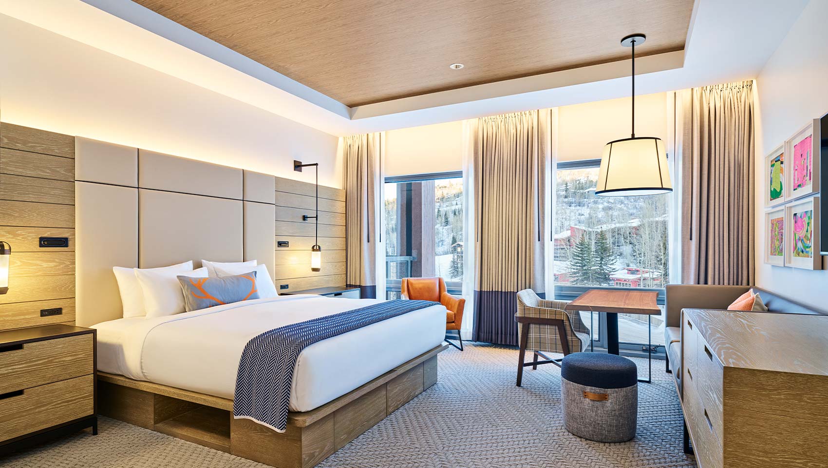 A neatly made bed with white linens in an elegant Limelight Snowmass room, featuring wooden furnishings, a seating area, and large windows.